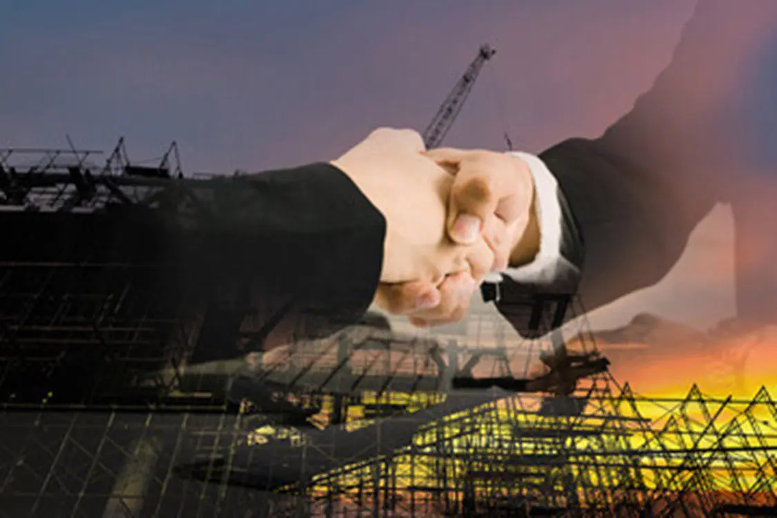         Description: Two business people shaking hands in front of a construction site undergoing printing works.